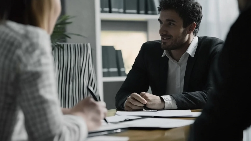 Smiling man in a business suit speaking with professionals at an office table during a meeting