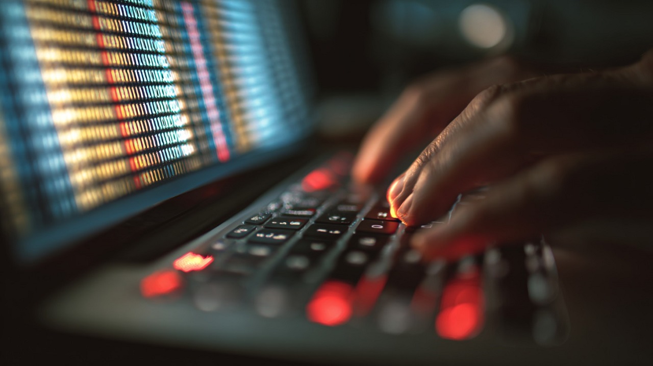 Close-up of hands typing on a keyboard, with colorful lines of data on a computer screen