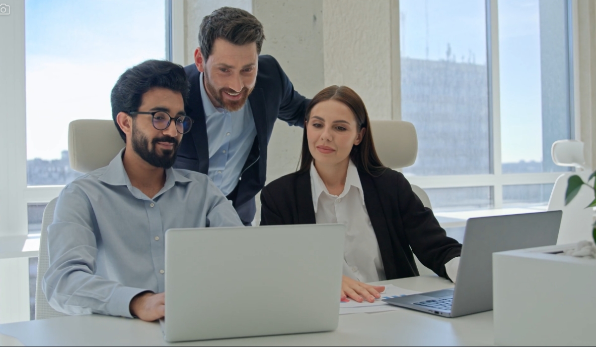 Three professionals working together on laptops in a modern office.